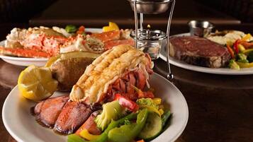 A dining table with plates of food including steak, lobster, and vegetables.