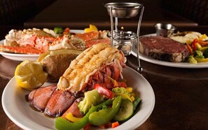 A dining table with plates of food including steak, lobster, and vegetables.