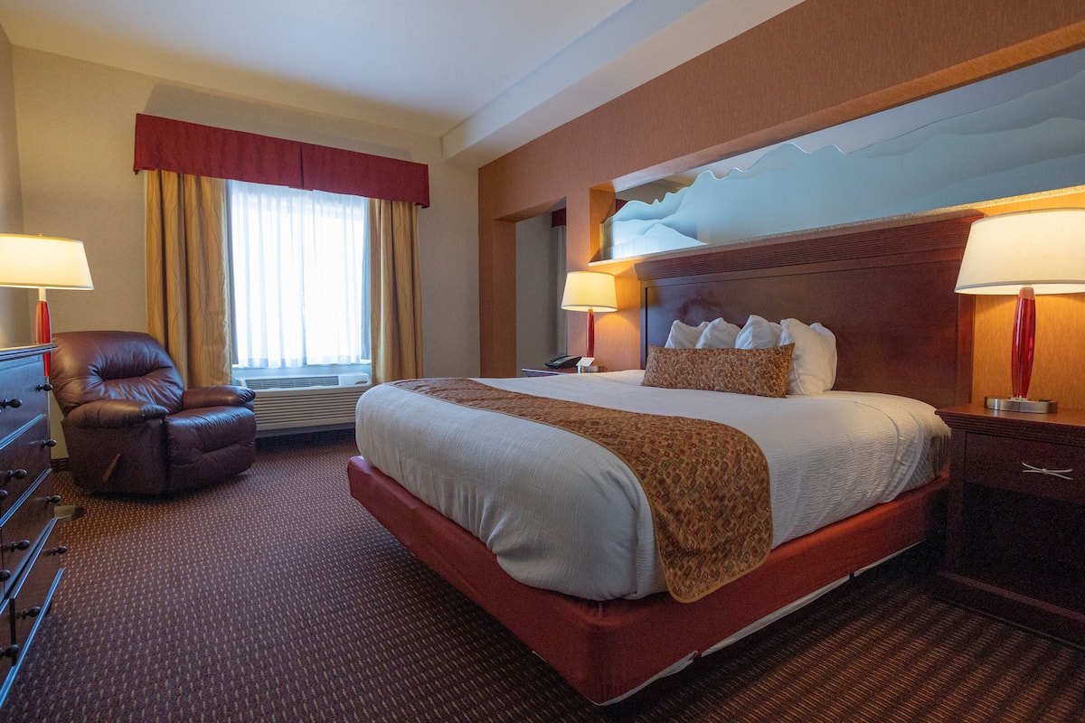 Una habitación de hotel con una cama grande, una silla, un escritorio y un cuadro en la pared.