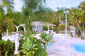 A pool area with a gazebo, surrounded by tropical plants and a statue.