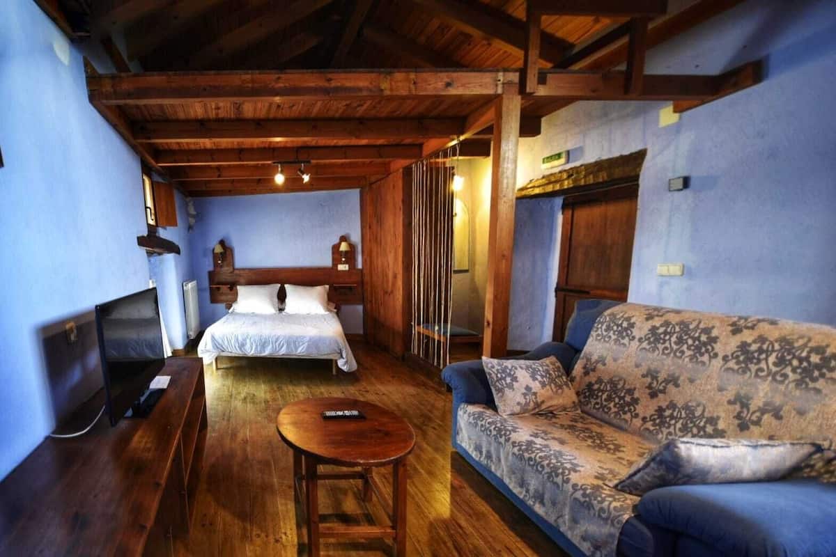 A room with a bed, a sofa, a wooden coffee table, and a television.