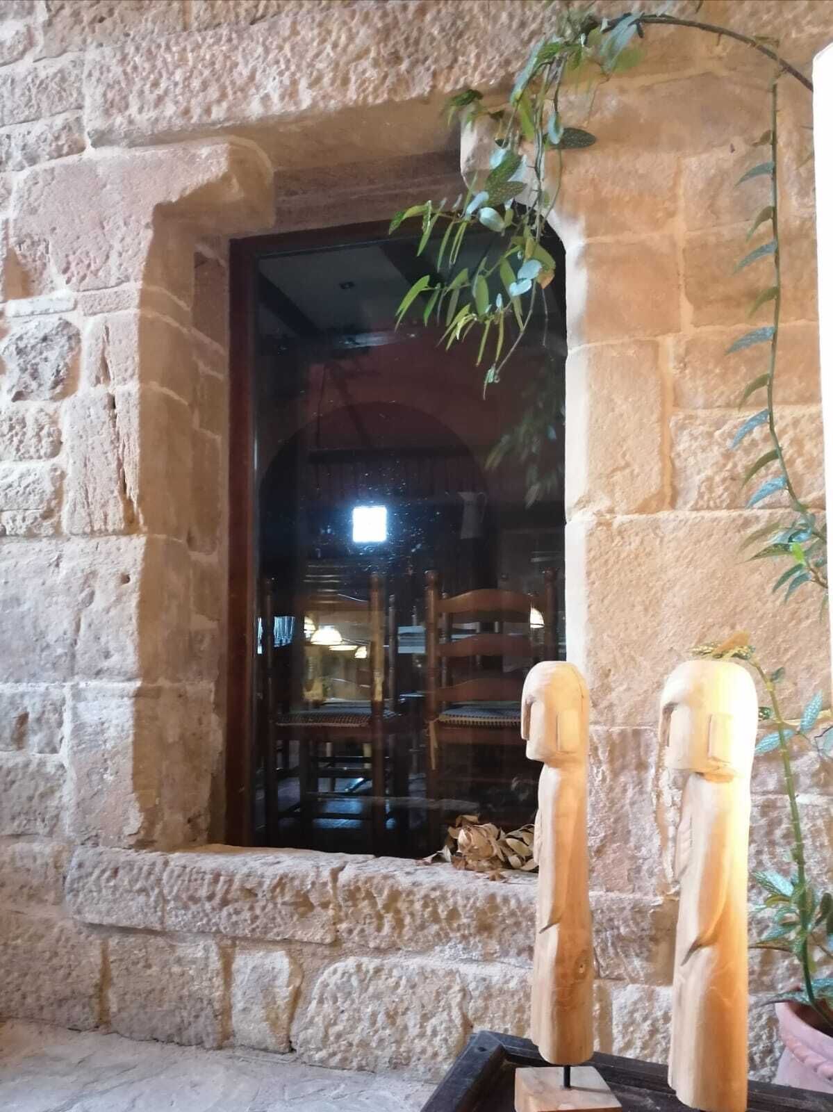 A stone archway with a wooden chair inside, a potted plant, and a wooden sculpture outside.