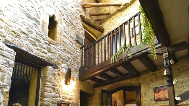 A stone courtyard with a wooden balcony, potted plants, and rustic furniture. - Palacio de Orisoain (Orísoain)