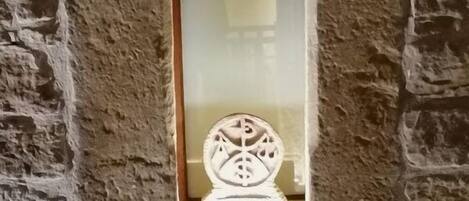 A stone wall with a narrow arched window featuring a decorative metal piece.