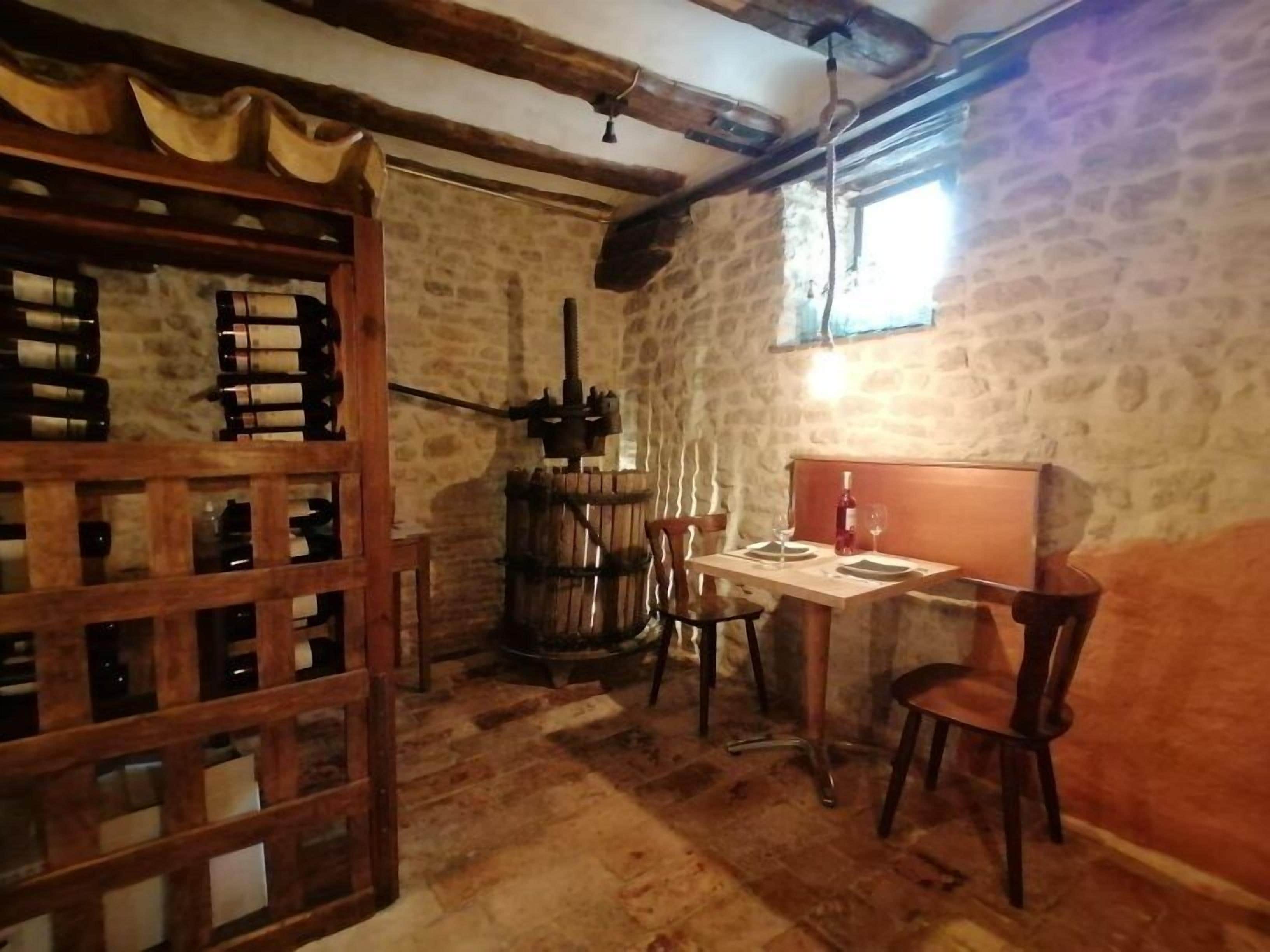 A rustic room with stone walls, wooden beams, a wooden table with chairs, and a wine rack.