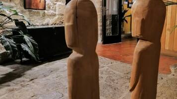 Two wooden sculptures in a stone-walled room with a television on the wall and a door leading to another room.