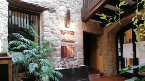 A stone-walled courtyard with a rustic bench, potted plants, and a wooden cabinet with decorative items. - Palacio de Orisoain (Orísoain)
