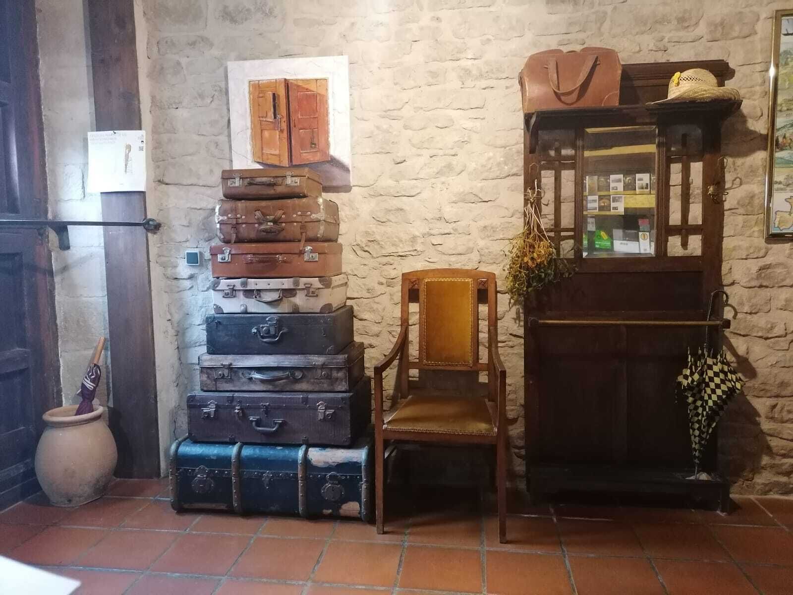 A rustic room with stacked vintage suitcases, a wooden chair, and a mirror with hanging items.