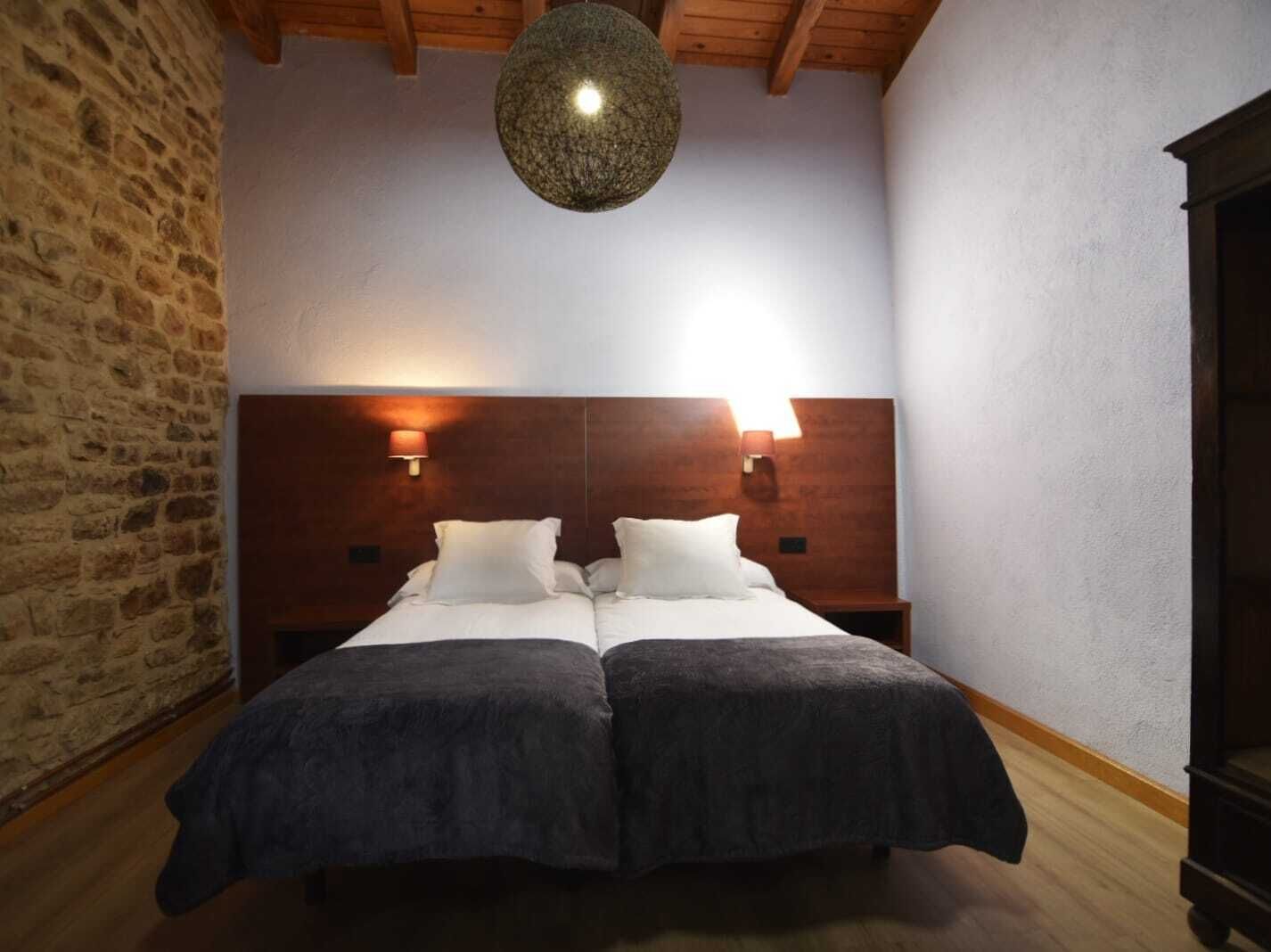Una cama doble con dos almohadas, cabecera de madera y dos lámparas fijadas a la pared.