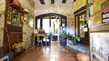 A rustic interior with stone walls, a wooden desk, a basket of dried flowers, and a pumpkin on the floor.