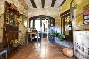 Un interior rústico con paredes de piedra, un escritorio de madera, una cesta de flores secas y una calabaza en el suelo.