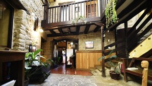 A stone-floored corridor with wooden beams, a wooden staircase, and potted plants. - Palacio de Orisoain (Orísoain)