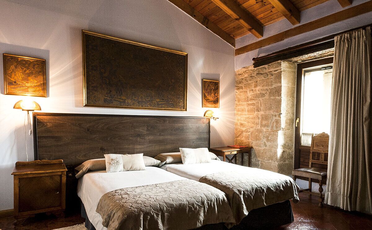A bedroom with a large bed, two bedside tables, a wooden headboard, and a stone wall.