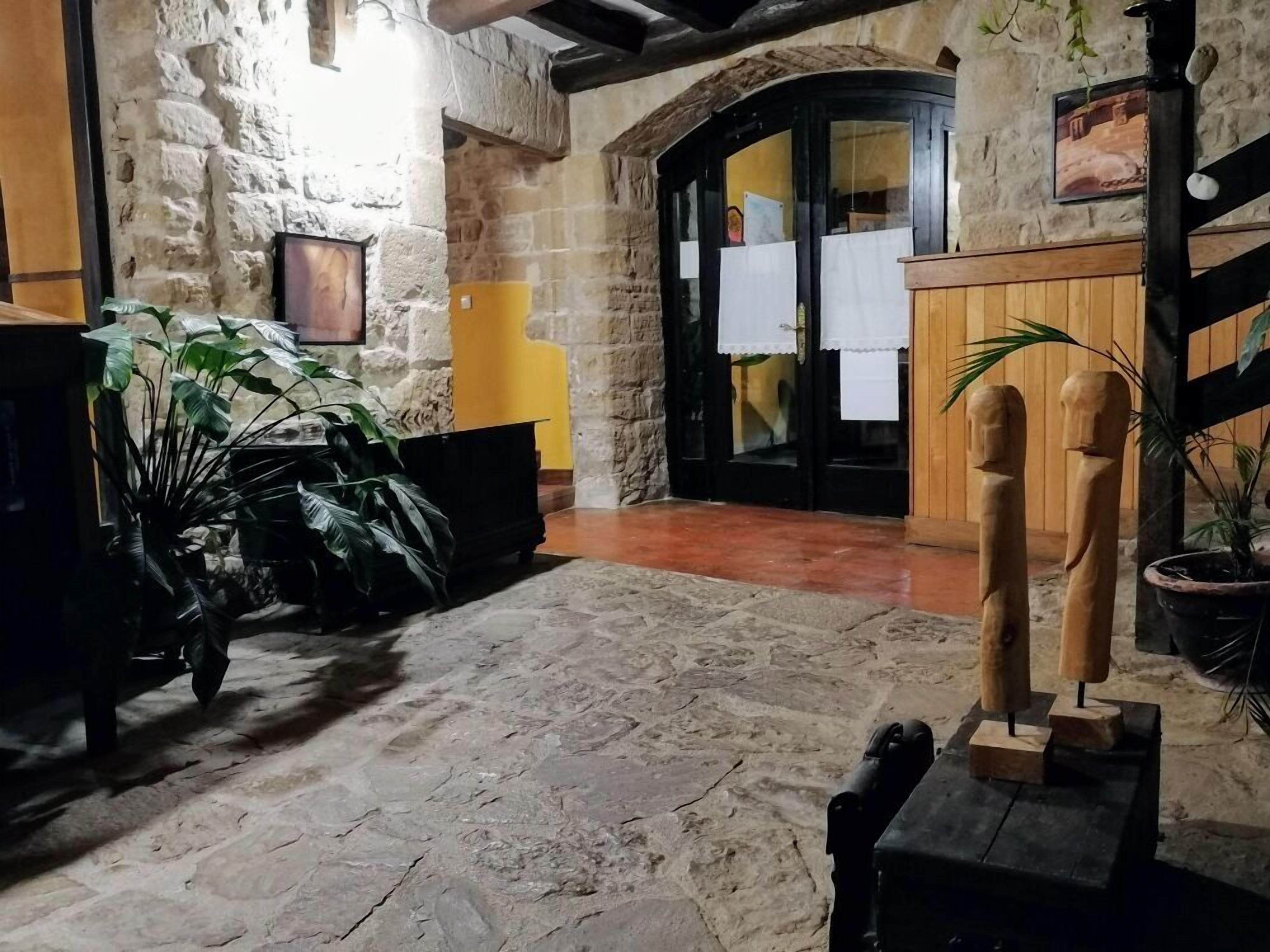 Un intérieur aux murs de pierre, avec un comptoir d’accueil en bois, des plantes en pot et une sculpture rustique en bois.