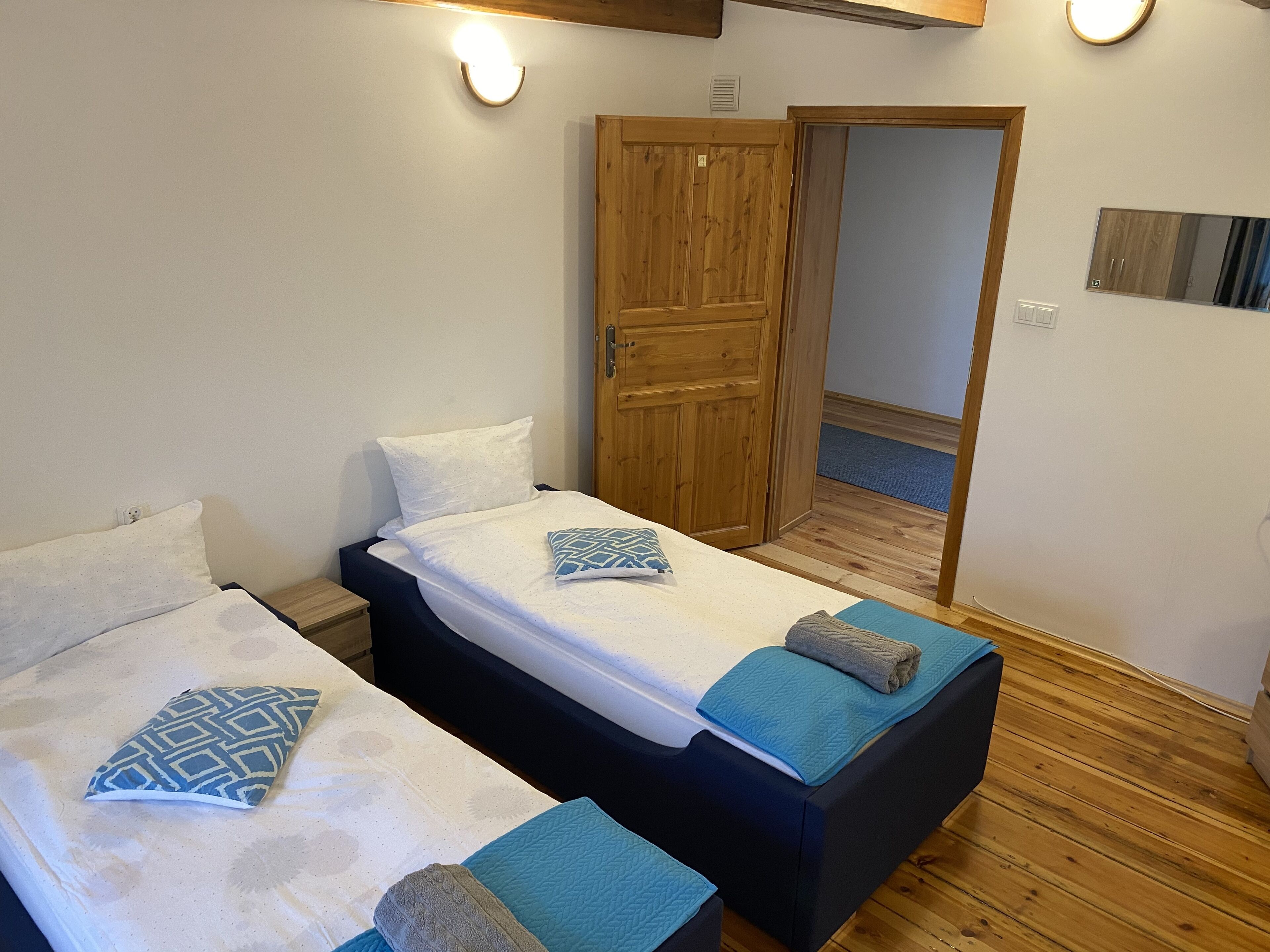 A room with two beds, wooden flooring, a wooden wardrobe, and a mirror on the wall.