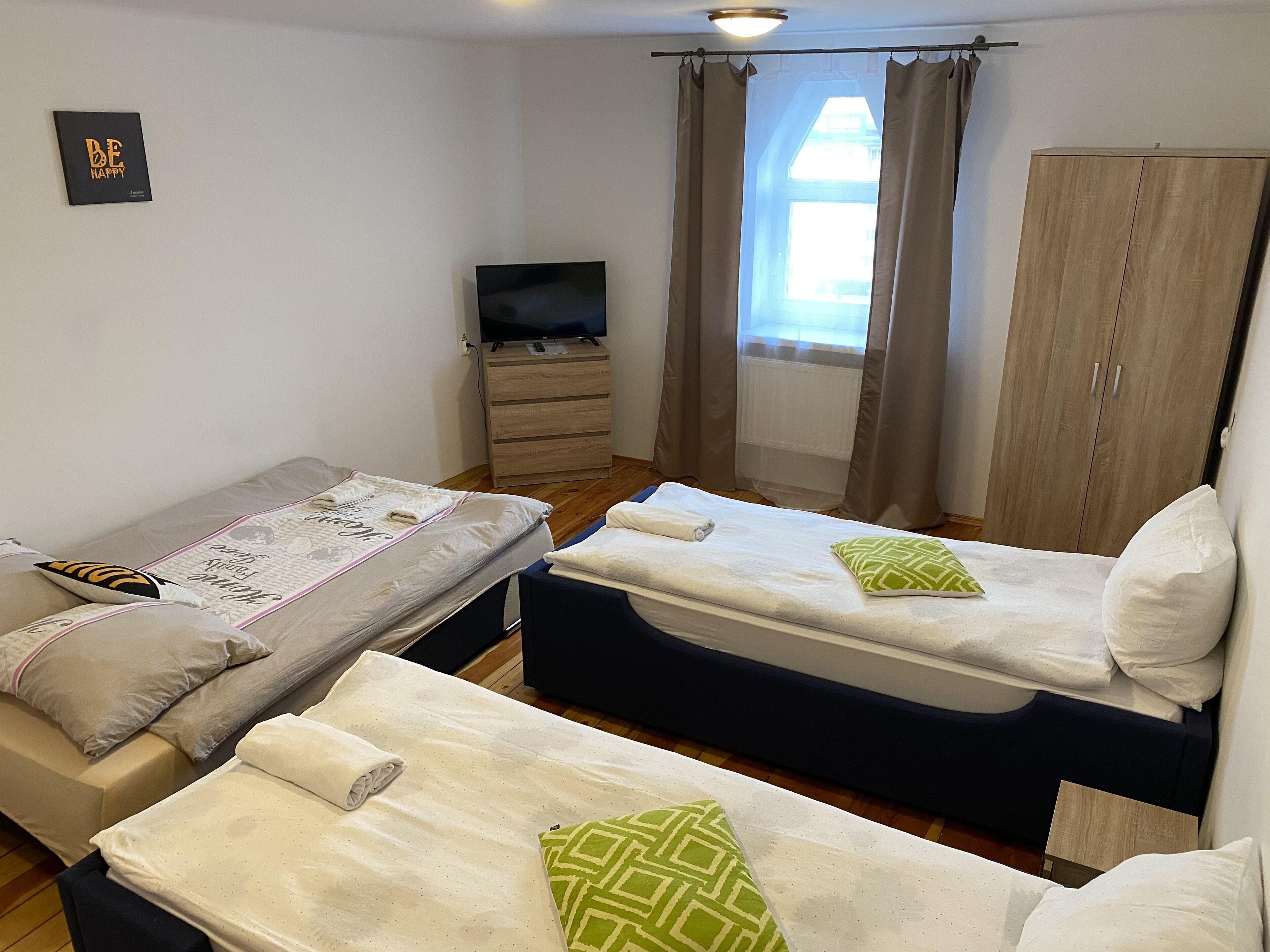 A room with two beds, a TV, a wardrobe, and a window with curtains.
