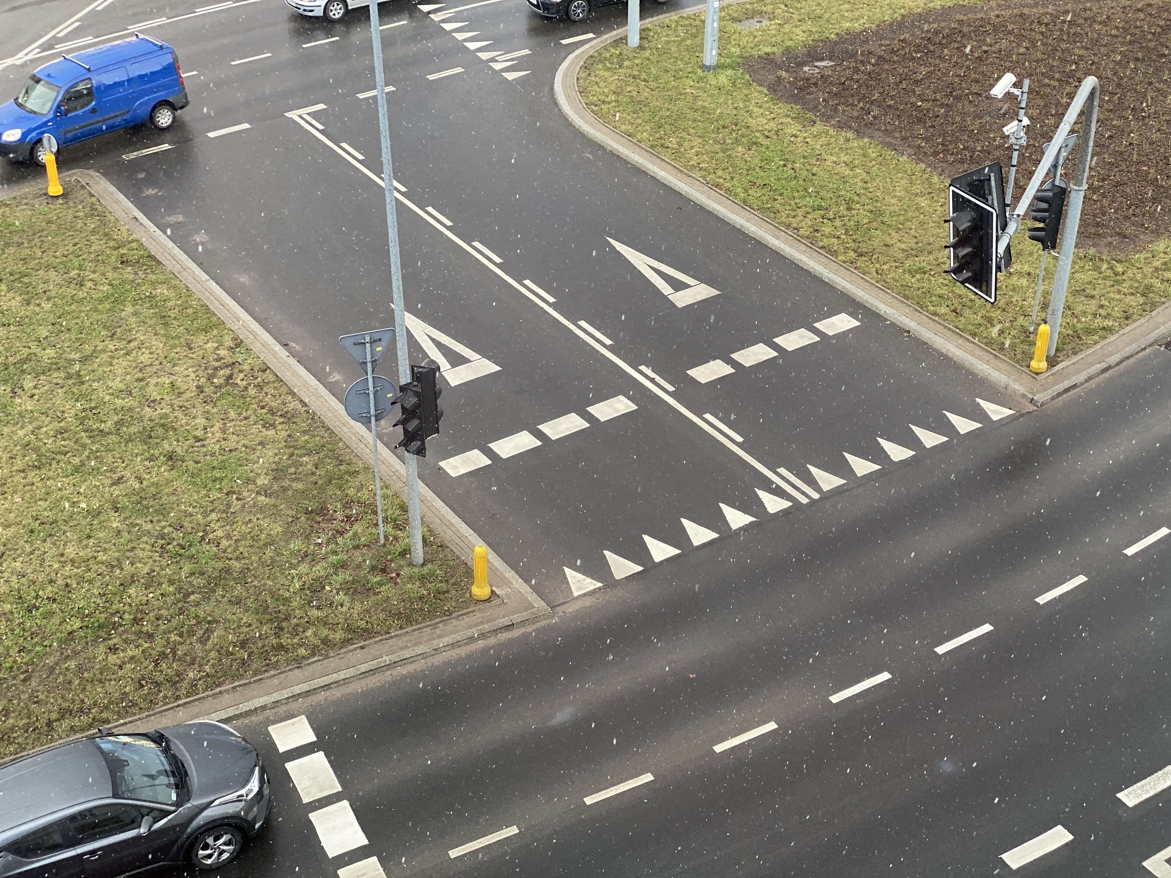 Vista aérea de una intersección con semáforos, marcas viales y una zona arbolada.