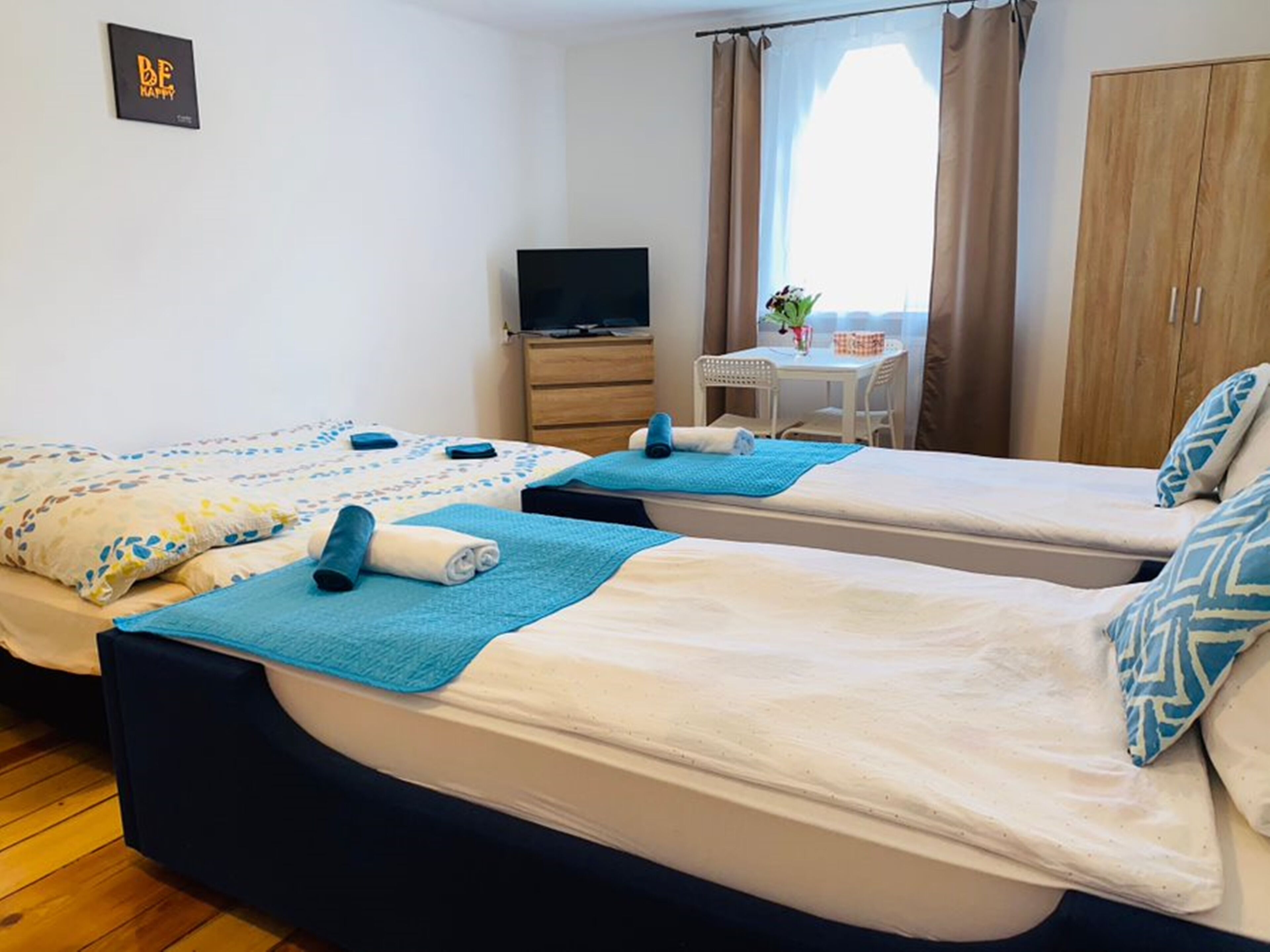 Una habitación de hotel con dos camas, un televisor, una mesita con una silla y un armario.
