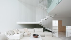Un interior moderno con un sofá blanco modular, una escalera de cristal y un diseño minimalista.
