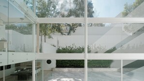 Un interior moderno con un sofá modular, paredes de vidrio y vistas al verde exterior.