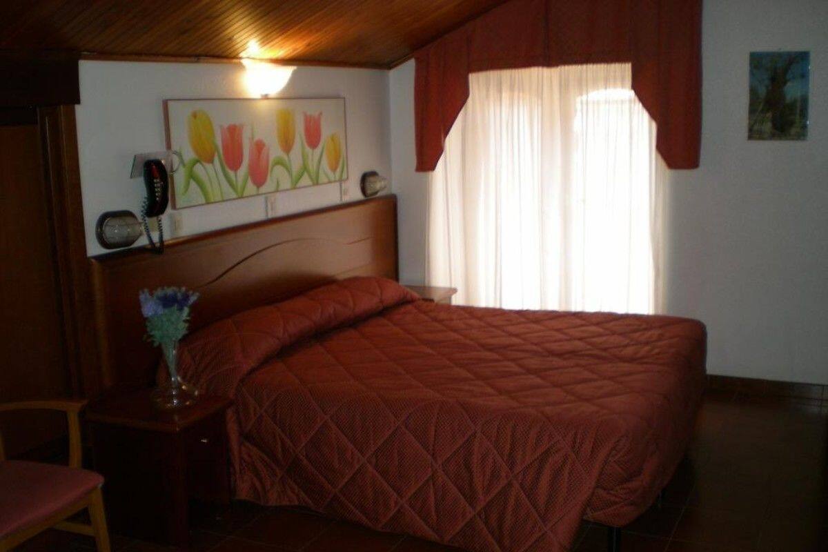A bedroom with a bed, a nightstand, a chair, a painting, and a window with curtains.