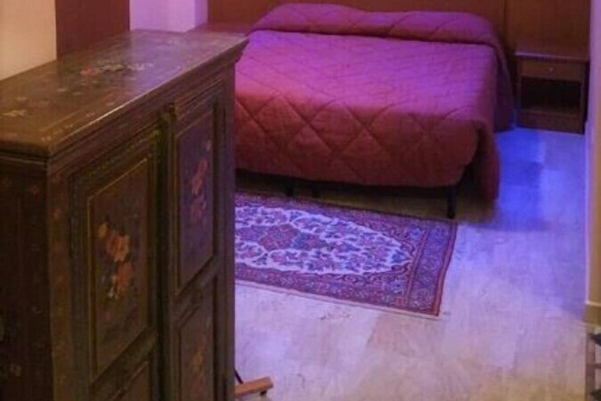 A bedroom with a bed, a dresser, a painting on the wall, and a patterned rug.