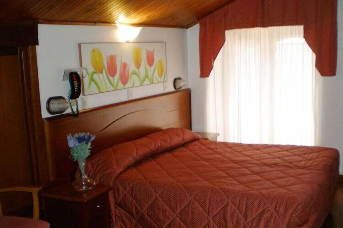 A bedroom with a wooden headboard, a quilted bedspread, a bedside table with a lamp, and a painting on the wall.