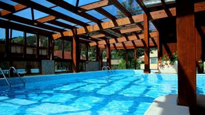 An indoor swimming pool with wooden beams and glass walls, surrounded by a covered area. - Hotel Cercone (Caramanico Terme)