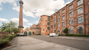 A large brick building with a tall chimney, a van parked in front, and a car parked on the side.