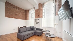 A modern living room with a grey sectional sofa, a small round table, and a large window with blinds.