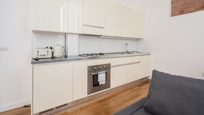 A compact kitchen with white cabinets, a stainless steel oven, and a countertop with a kettle and toaster.