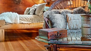 A cozy room with a wooden floor, a glass table with a decorative box, a wicker chair with a fur throw, and a patterned lamp.