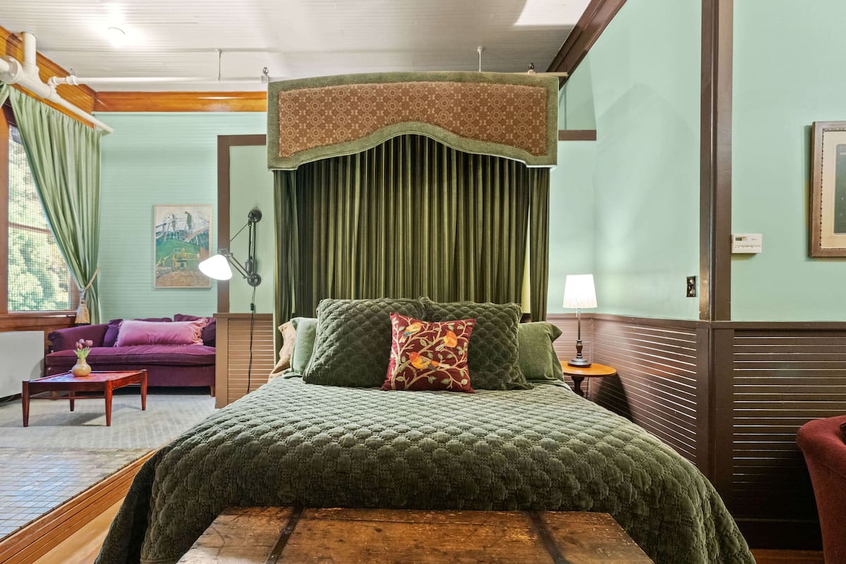 Una habitación con una cama, una mesita de noche, una lámpara, una silla y un cuadro en la pared.