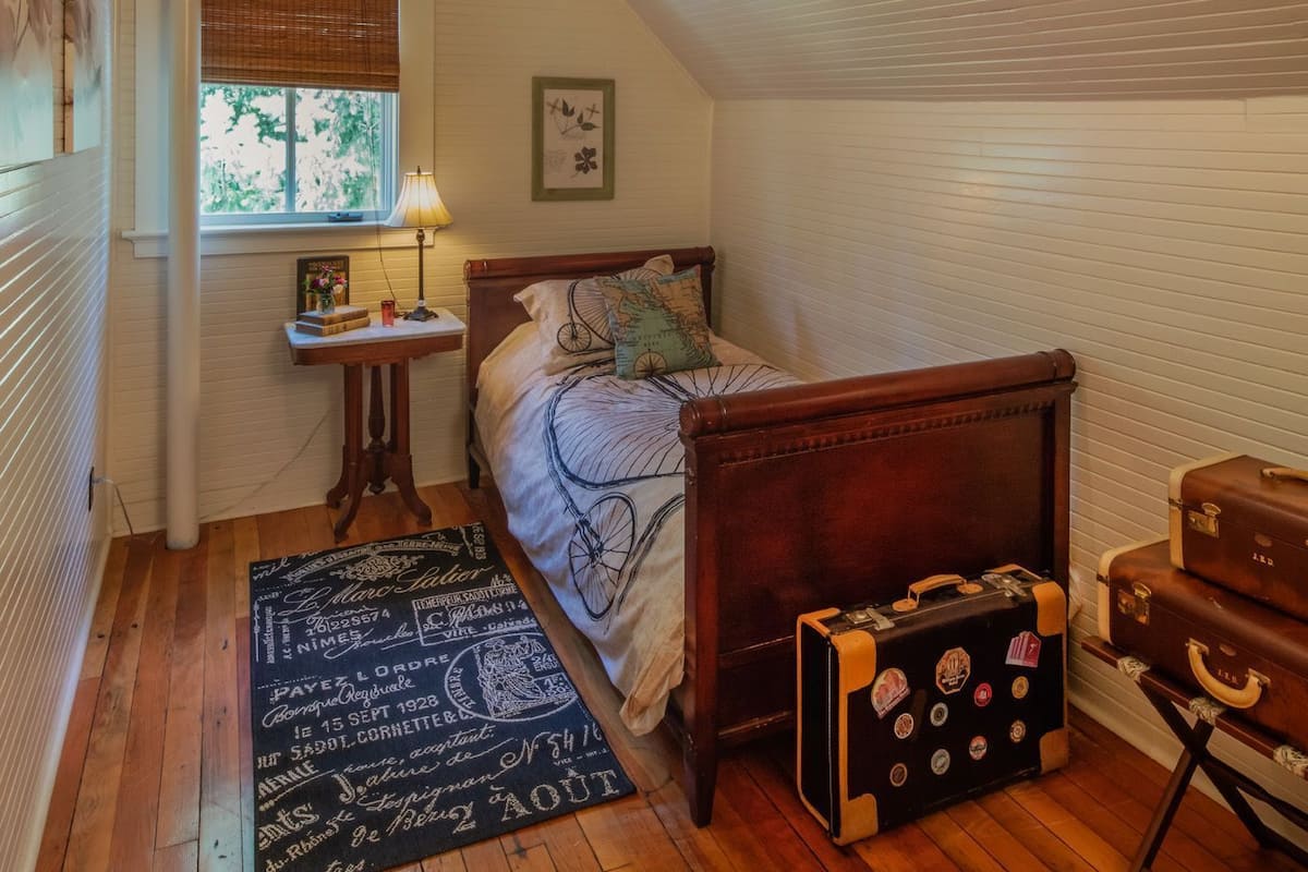 Un dormitorio con una cama de madera, una mesita de noche, una lámpara, una maleta y una ventana con persianas.