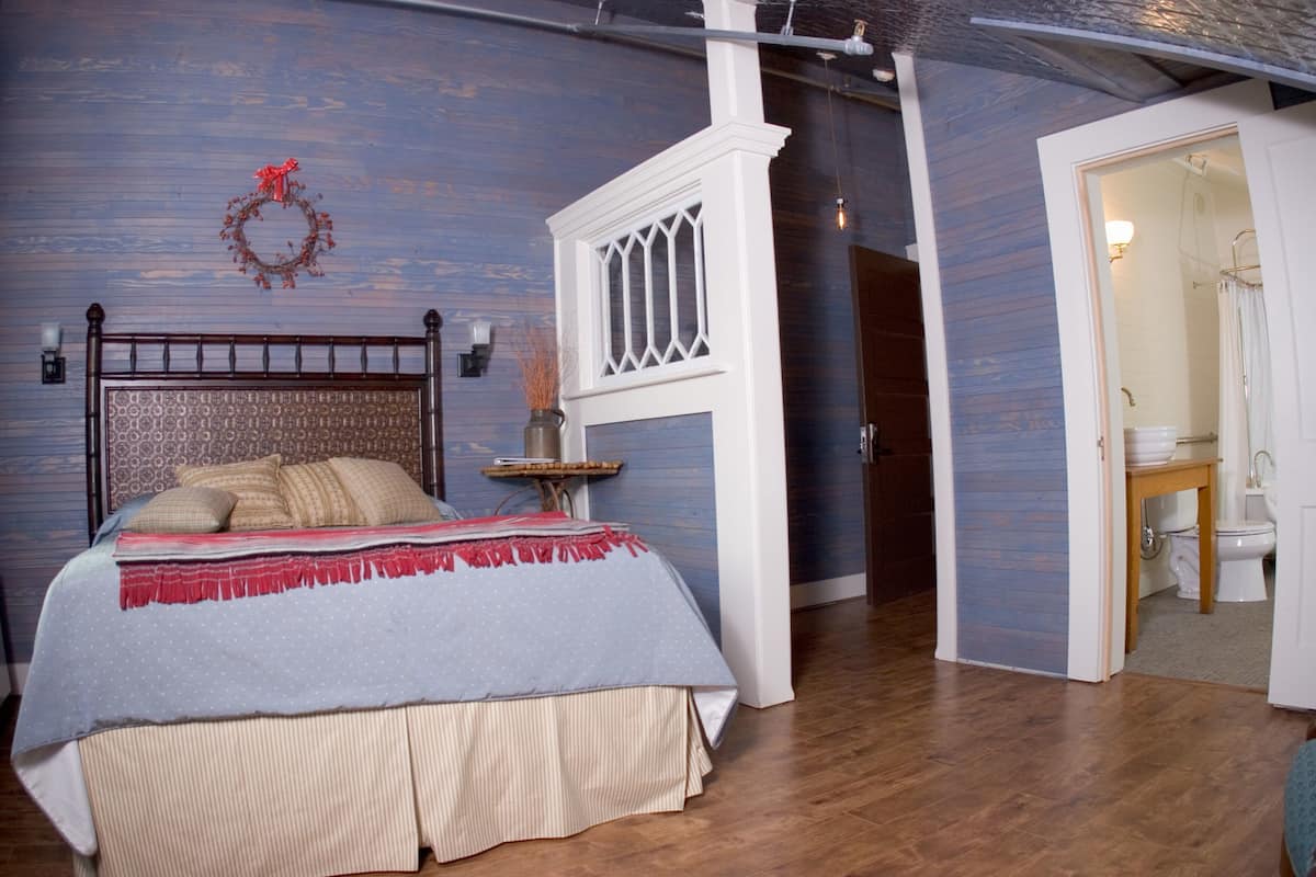 Un dormitorio con cama, cómoda, mesita de noche, lámpara de pared y puerta que da a un baño.