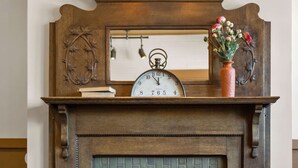 A fireplace with a clock above it, a vase with flowers, and a book on the mantel.