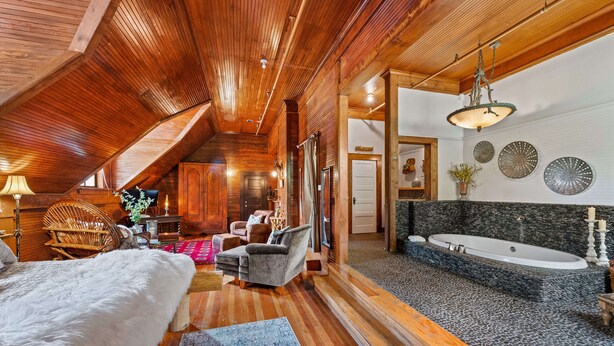 A spacious room with a wooden ceiling, a large window, a cozy seating area with a fur rug, and a modern bathroom with a large bathtub and decorative plates on the wall.