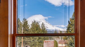 A view through a window of a mountain with a snow-capped peak, surrounded by trees and a clear sky.