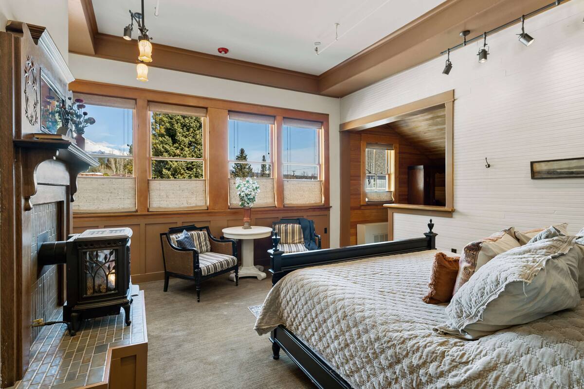 Un dormitorio acogedor con una cama grande, una chimenea, un rincón con asiento junto a la ventana y vistas al exterior.