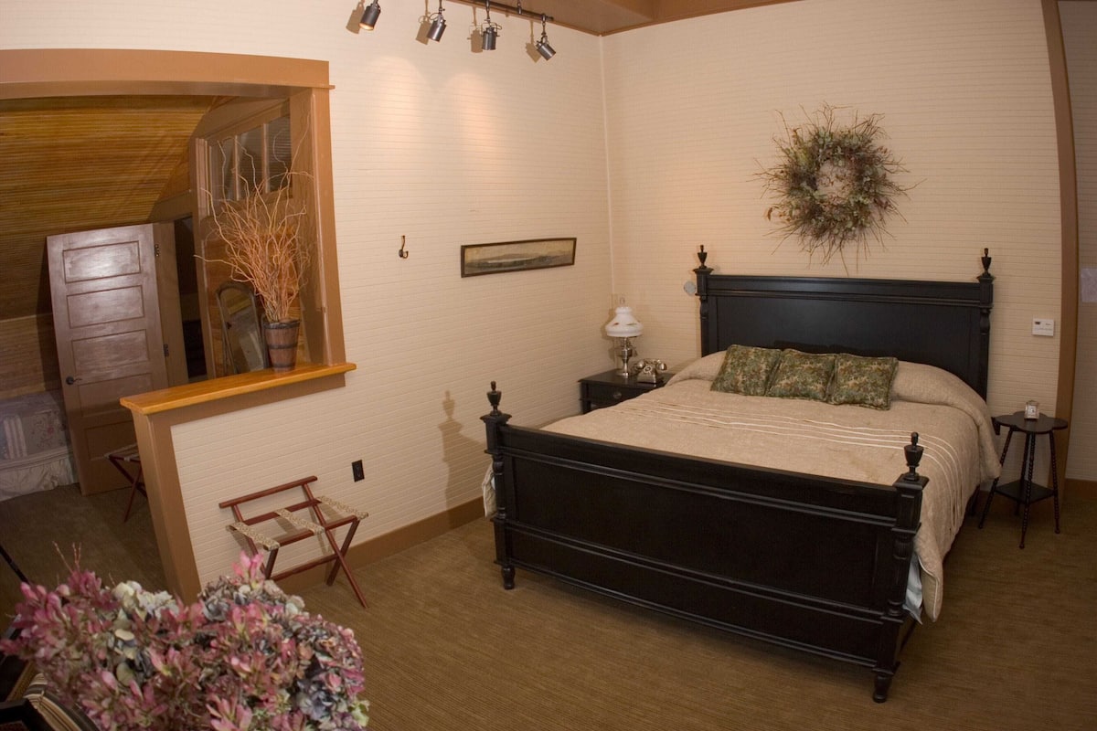 Un dormitorio con cama, mesitas de noche, lámpara, espejo, cómoda de madera y una planta decorativa.