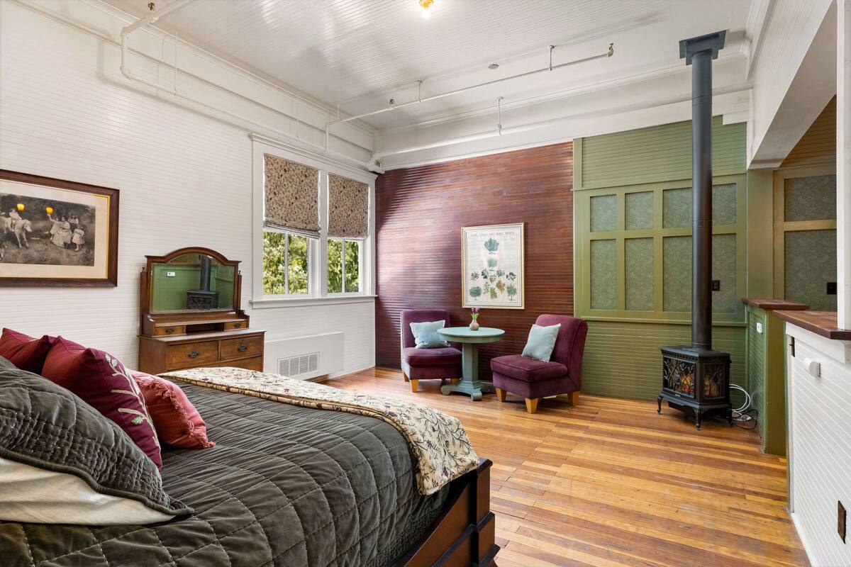 Una habitación acogedora con cama, dos sillones, una mesa, chimenea y ventana con persianas.