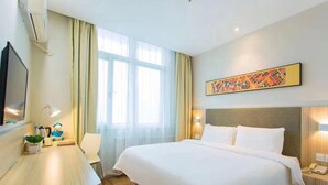 A hotel room with a bed, bedside table, lamp, and a painting on the wall.