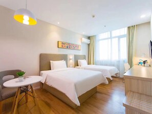 A hotel room with two beds, a desk, a chair, a small table, and a hanging lamp. - Hanting Hotel (Ürümqi)