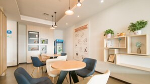 A modern cafe with round tables, blue and white chairs, a refrigerator, and a wall with a coffee-related poster.