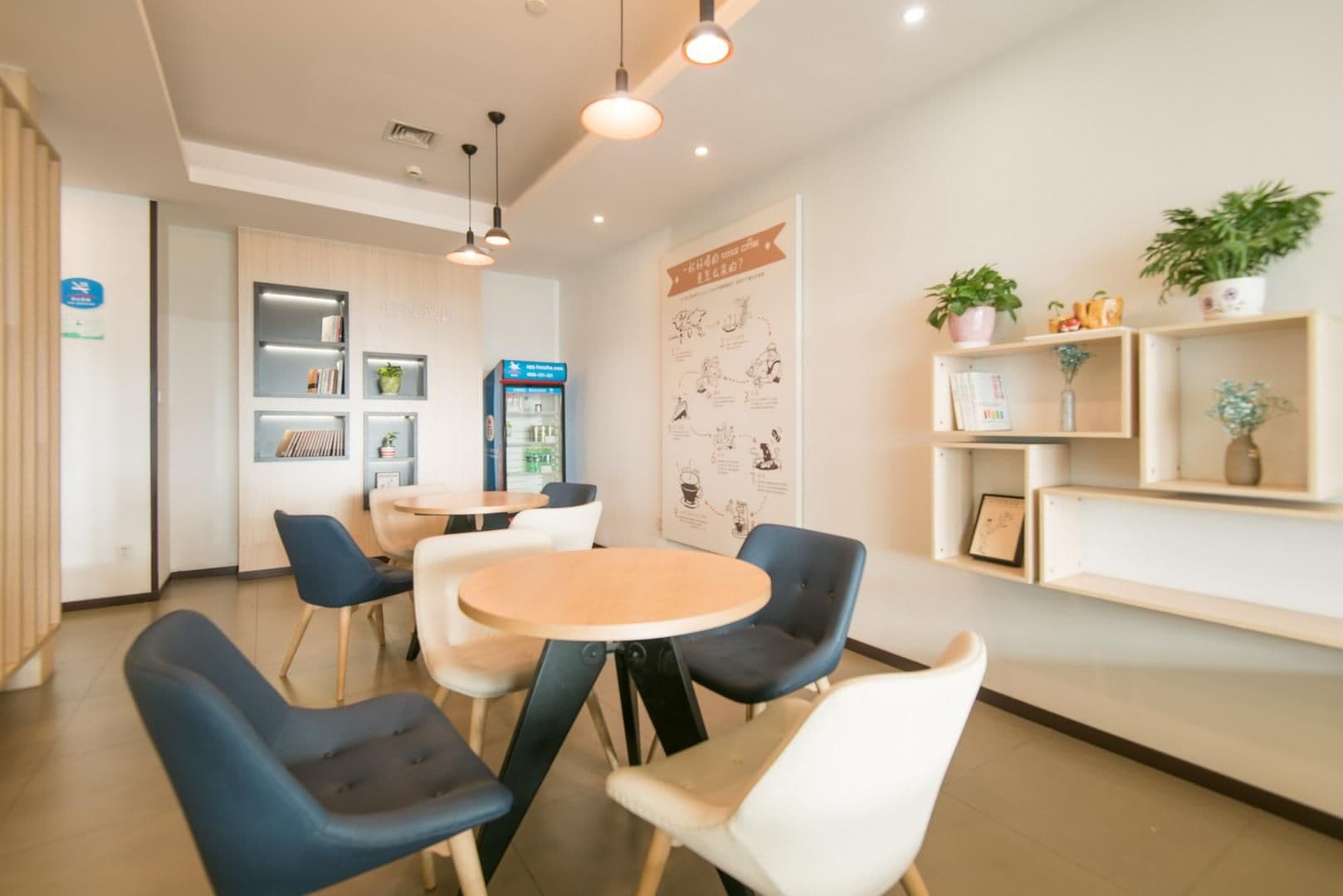 Un café moderno con mesas redondas, sillas azules y blancas, un refrigerador y una pared con un cartel sobre café.