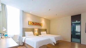 A hotel room with two beds, a desk, a chair, a painting on the wall, and a bathroom visible through an open door.
