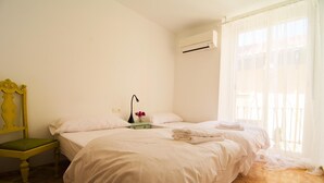 A hotel room with two beds, a chair, an air conditioning unit, and a window with sheer curtains. - Pensión San José (Granada)