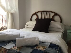 A neatly made bed with white bedding and a dark brown pillow, a quilt with a geometric pattern, and a wooden headboard. - Pensión San José (Granada)