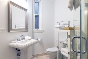 Un baño moderno con un lavamanos blanco, un inodoro, una ducha con mampara de vidrio y un espejo con marco decorativo.
