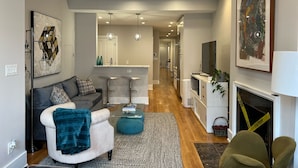 A modern living room with a sofa, a coffee table, and a TV. There is a kitchen area with a dining table and chairs. The room has a high ceiling with recessed lighting. - Dupont 5-Star, Walk Score 94, Metro, 2BR (Washington)